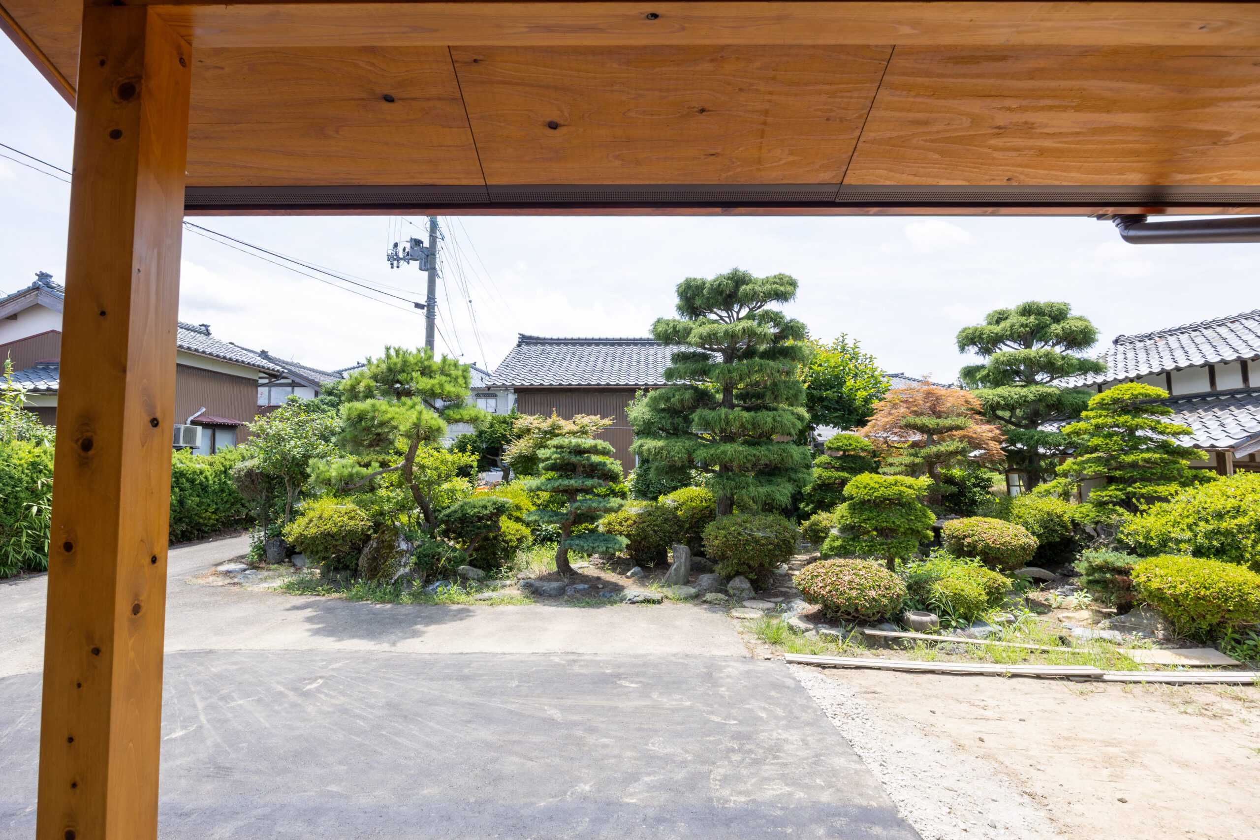 手入れされた松や庭木が並ぶ和風庭園を、軒下から見た眺め